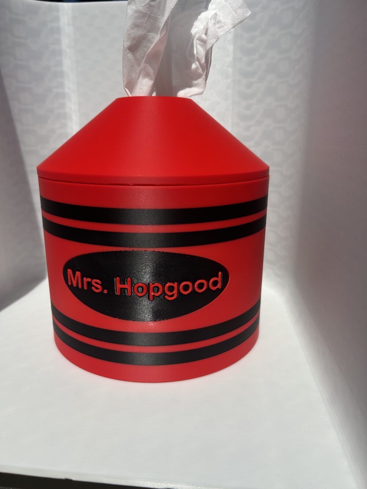 Red 3D printed crayon tissue box cover with a teacher name on the black label