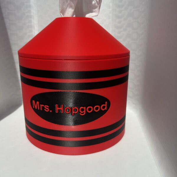 Red 3D printed crayon tissue box cover with a teacher name on the black label