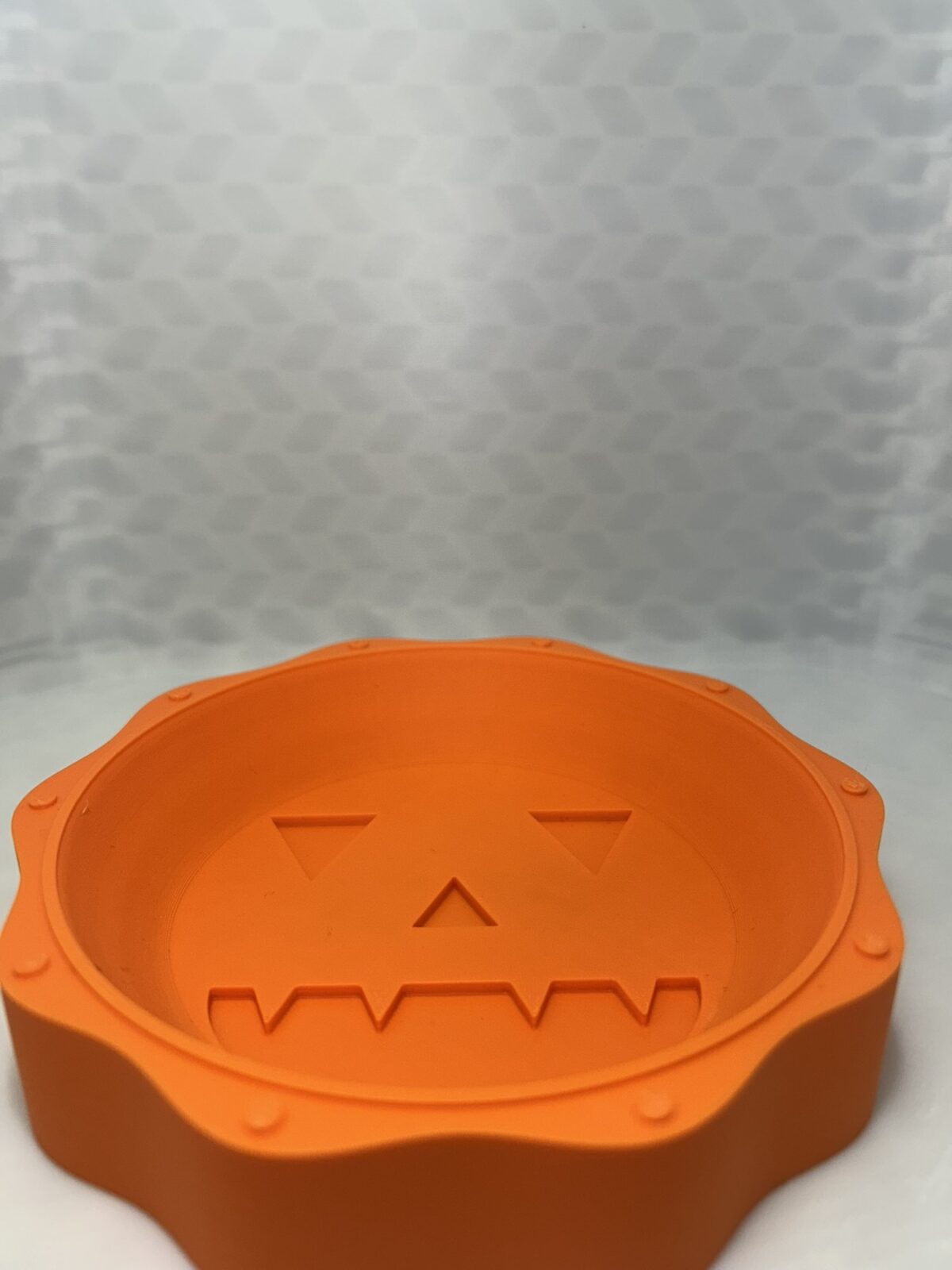 Orange 3D printed jack-o-lantern candy bowl with a carved face in the base