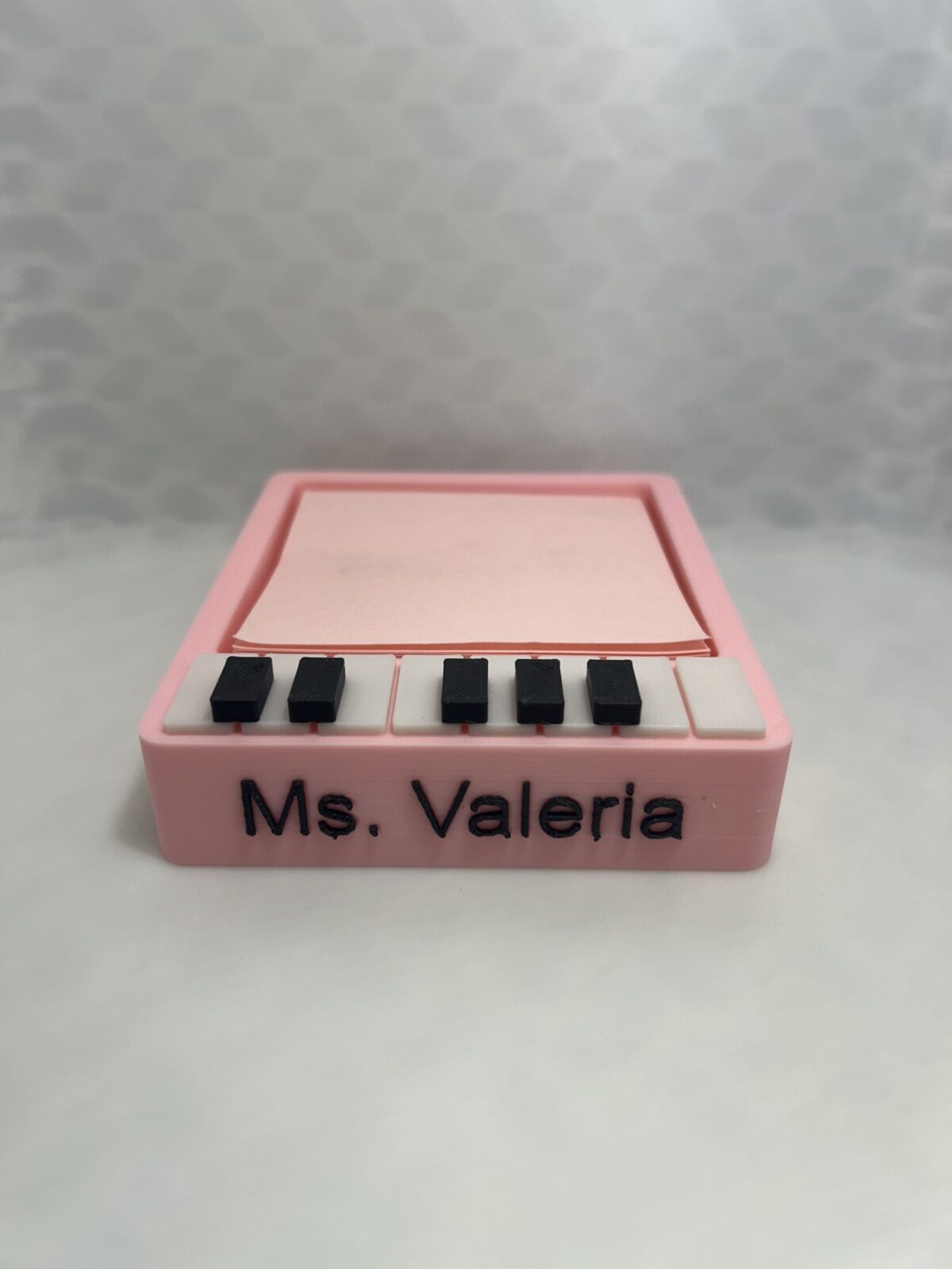 Pink 3D printed piano sticky note holder with black and white keys and the name Ms. Valeria